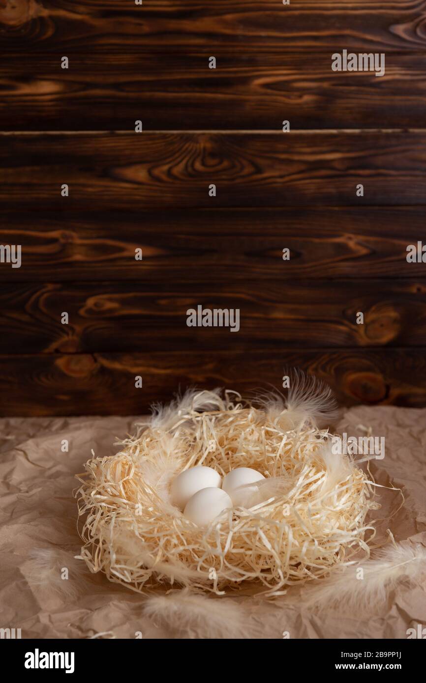 Chicken eggs lie on a wicked paper straw in a wicker basket on a dark wooden background in the morning sun Stock Photo