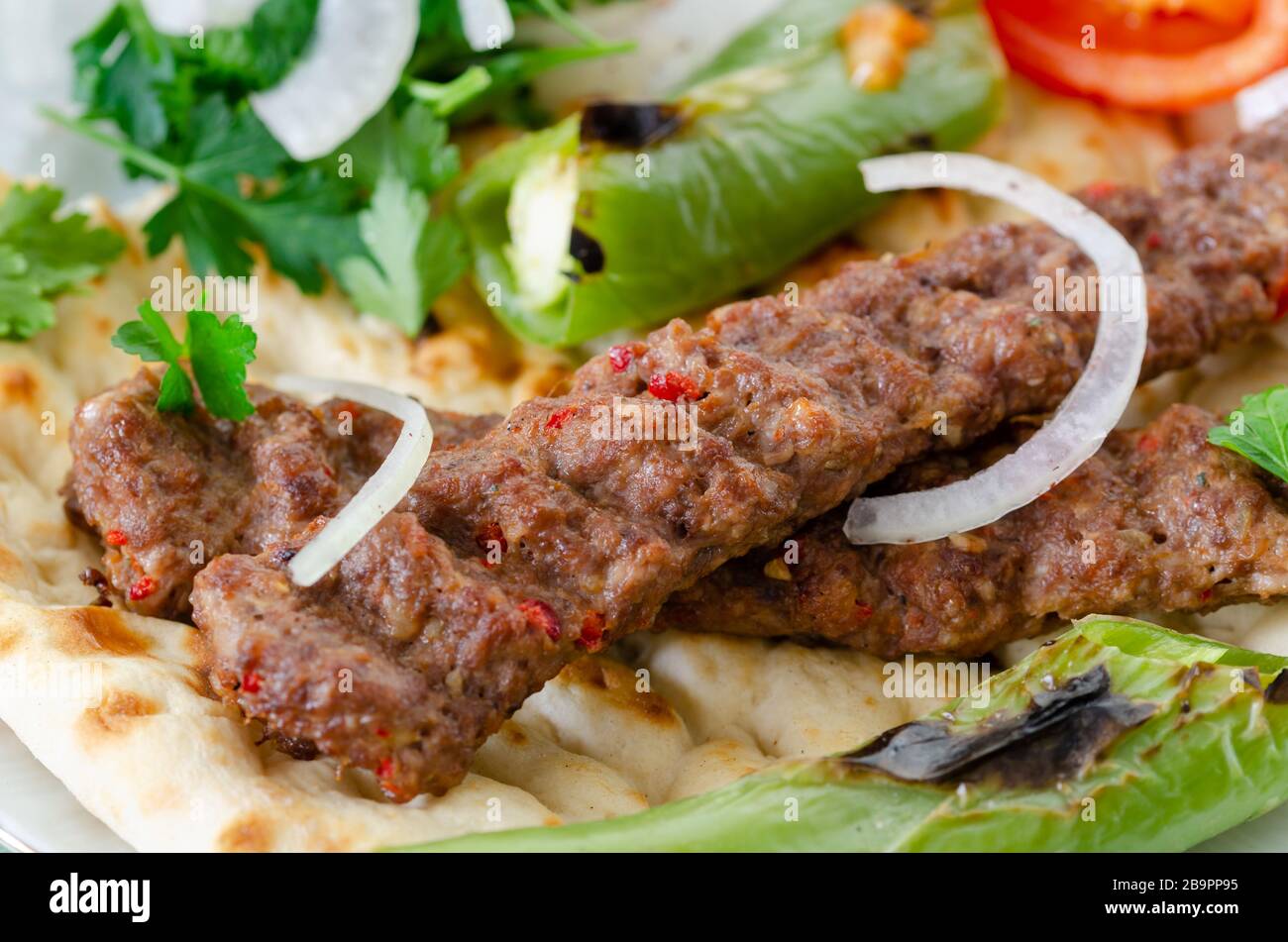 Traditional Adana Kebap with tomato and salad on a flatbread as top view. Stock Photo