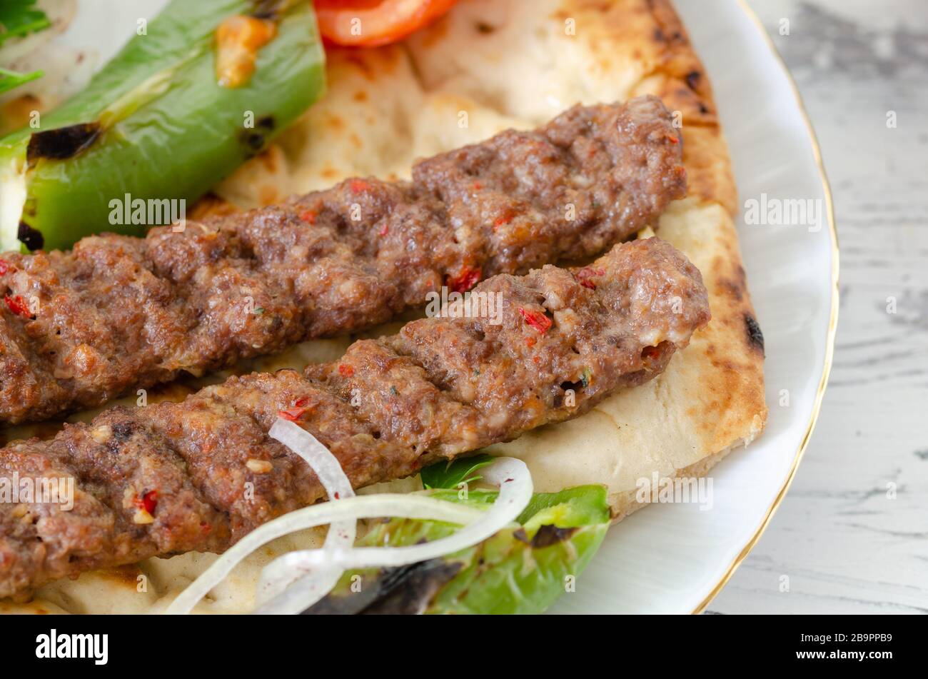 Traditional Adana Kebap with tomato and salad on a flatbread as top view. Stock Photo