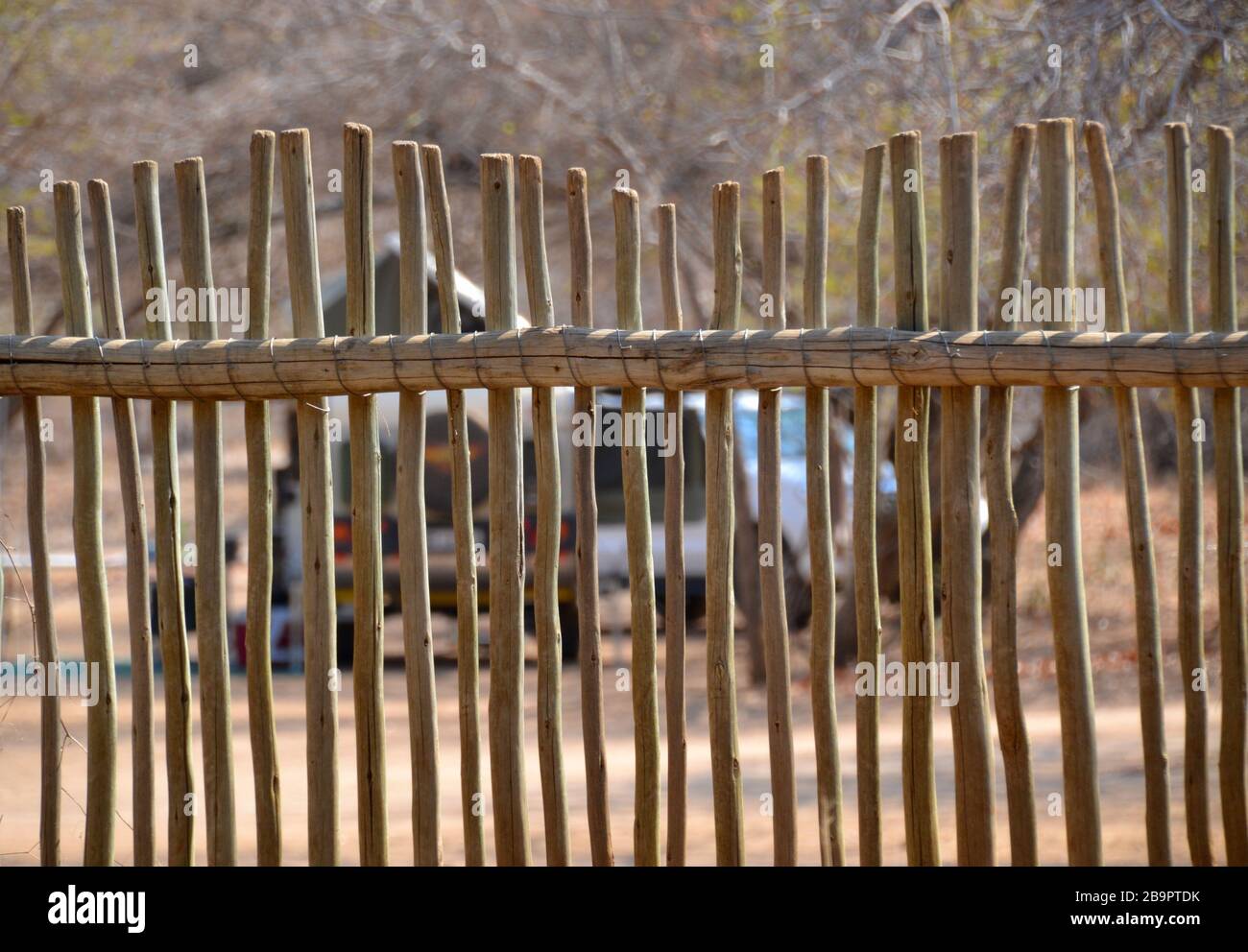 Uneven wooden game reserve fence at a camp site in Kruger National Park with a safari vehicle and tent visible in the background Stock Photo