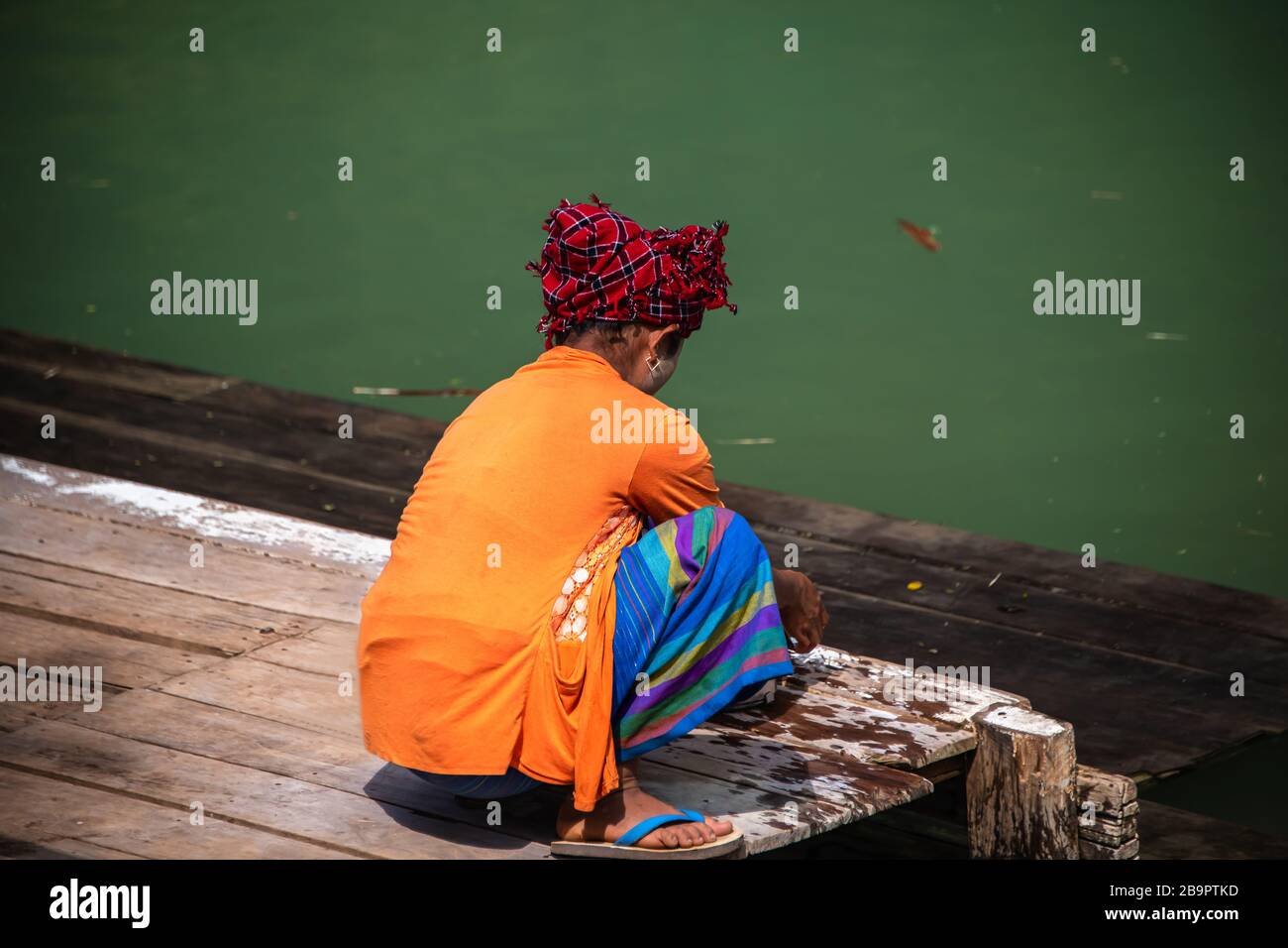 Local Intha Tribeswoman hand washing clothing on a river bank, Inle Lake, Myanmar. Rear view portrait of an woman against a water background Stock Photo