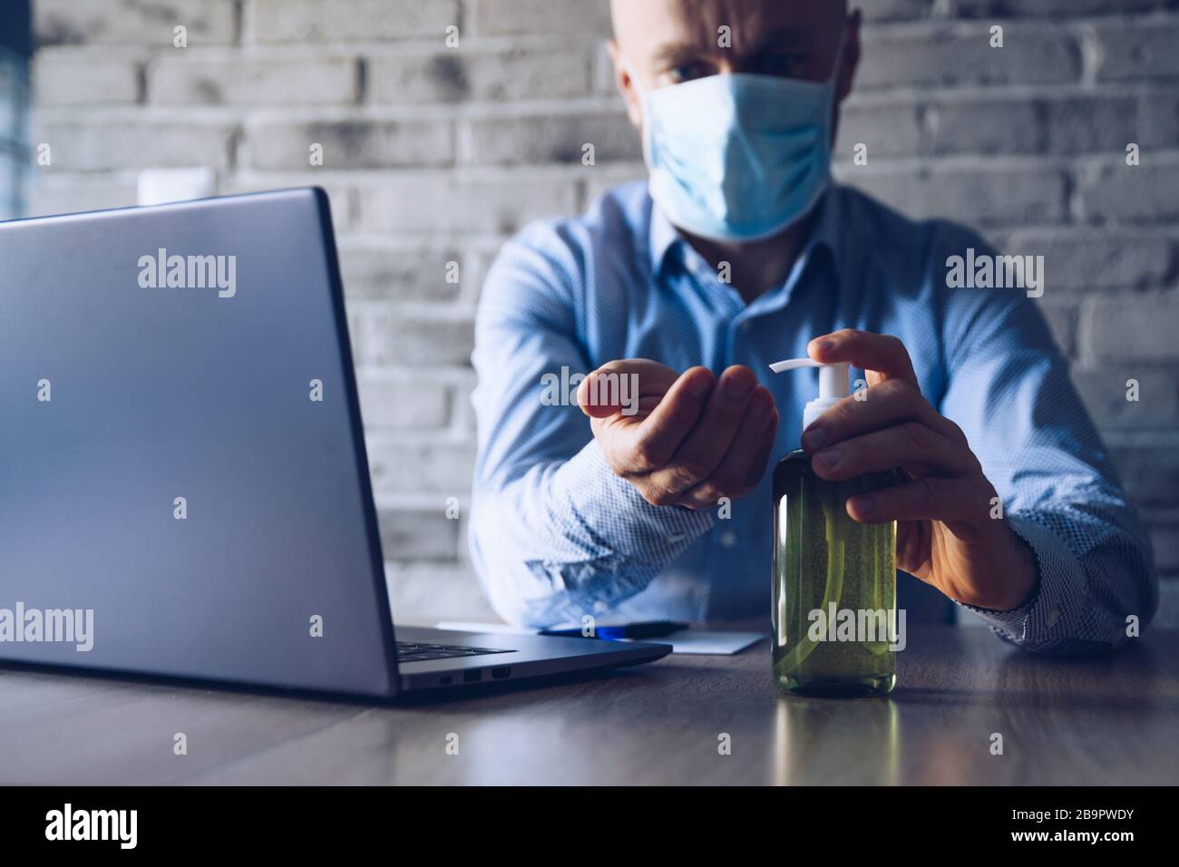 Man in an office using a computer and disinfects his hands with ...