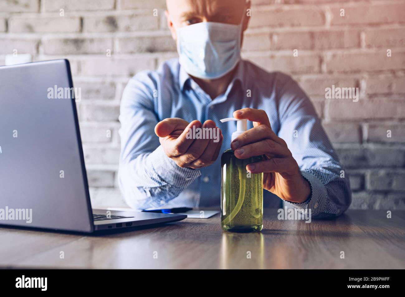 Man in an office using a computer and disinfects his hands with ...
