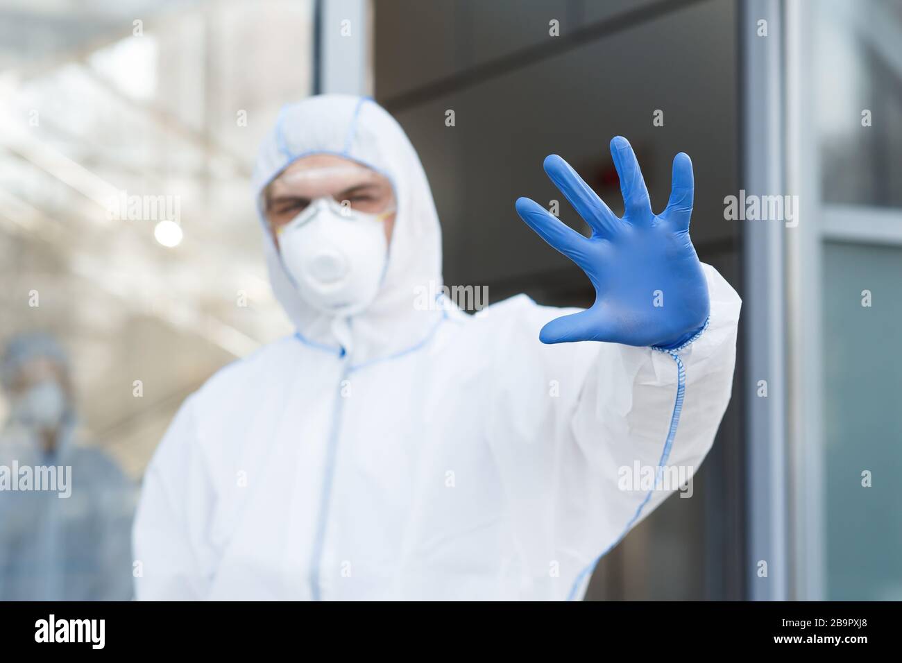 Man in virus protective suit and mask gesturing to stop world epidemic Stock Photo