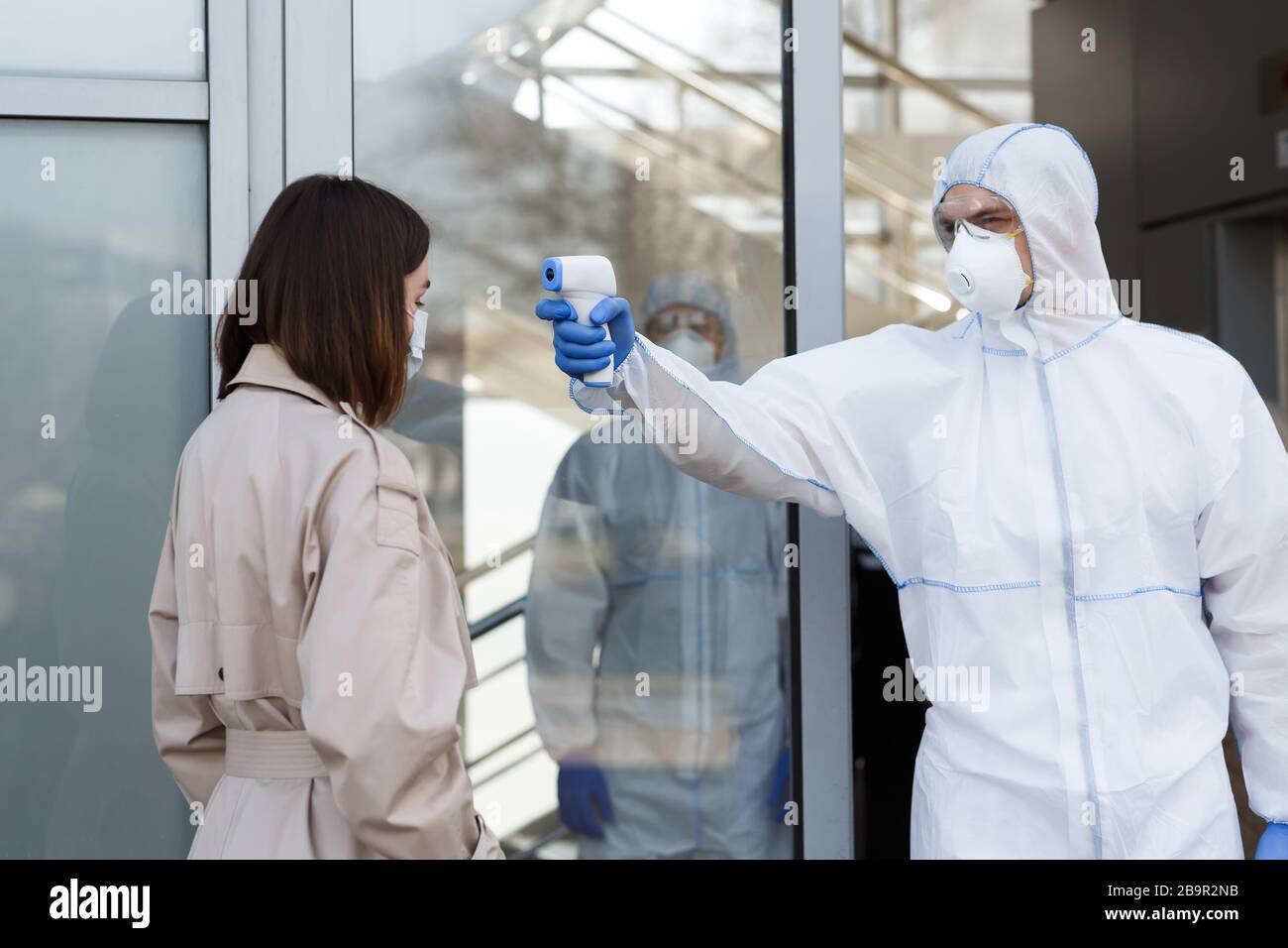 Man in coronavirus hazmat measuring temperature of a woman Stock Photo