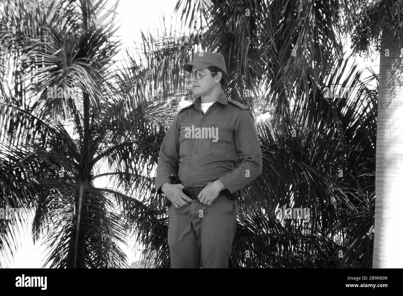 smart military Soldier on guard with sun glasses in Cuba with palm trees in rear military army hat gun palm trees tree palms watch watching Stock Photo