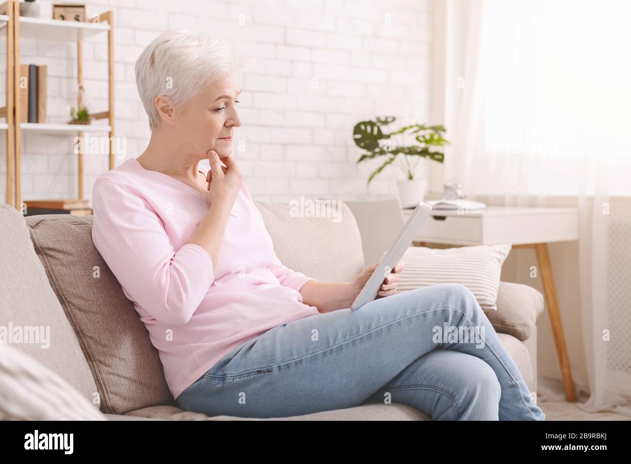 Worried senior woman reading Covid-19 news articles Stock Photo