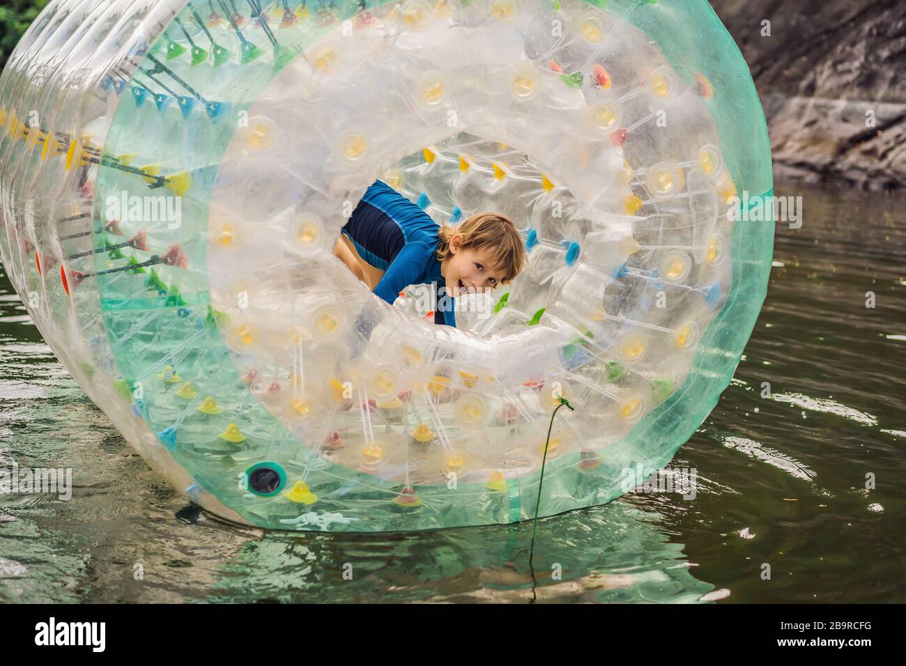 Cute little boy, playing in Zorb a rolling plastic cylinder ring with a hole in the middle on the lake Stock Photo