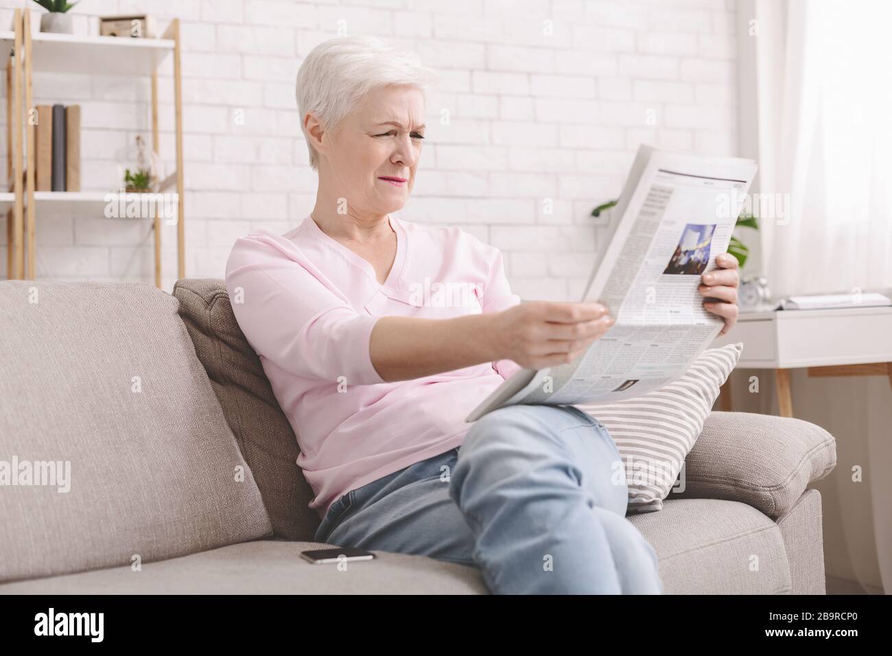 Senior lady squinting and holding newspaper far from eyes Stock Photo