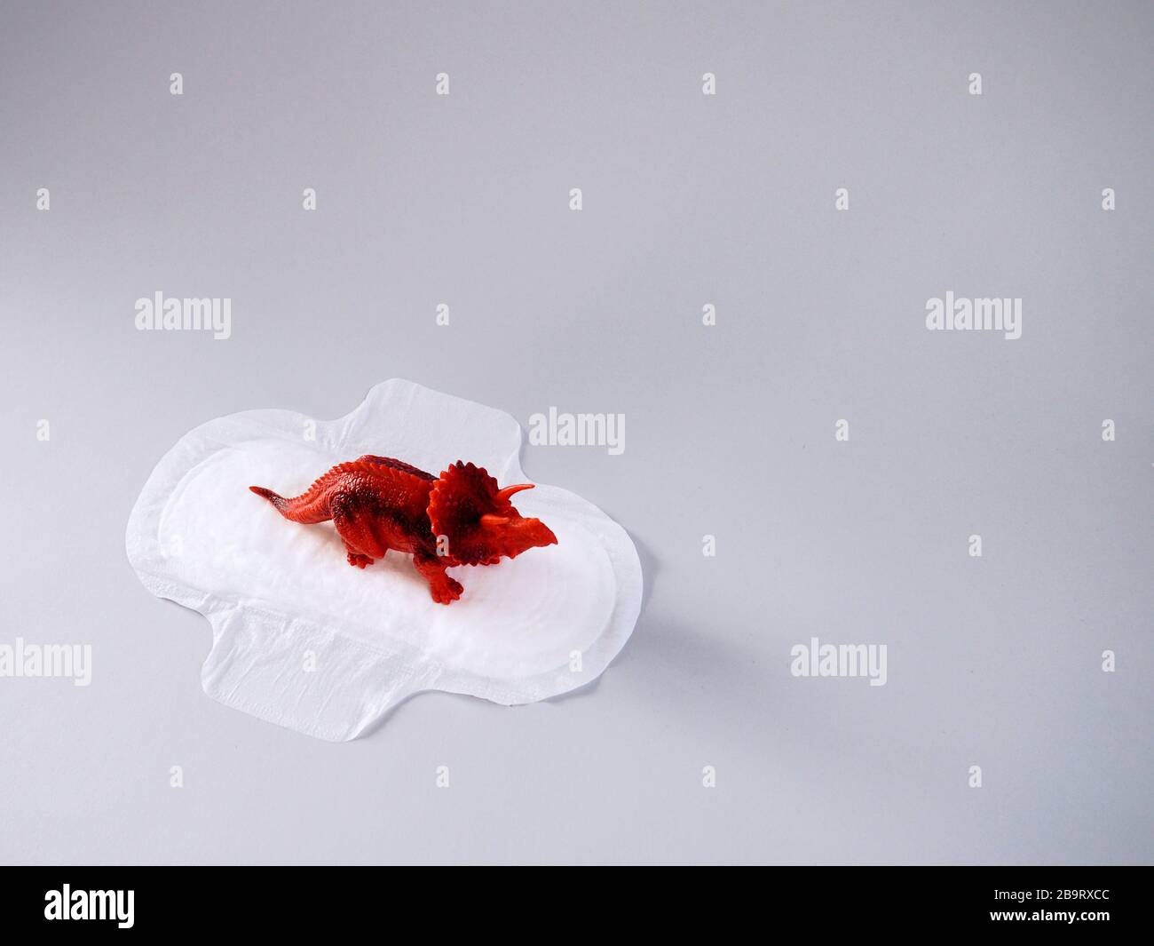 Menstrual pad with red triceratops on gray background. Minimalist still life photography concept. Women critical days, gynecological menstruation cycl Stock Photo