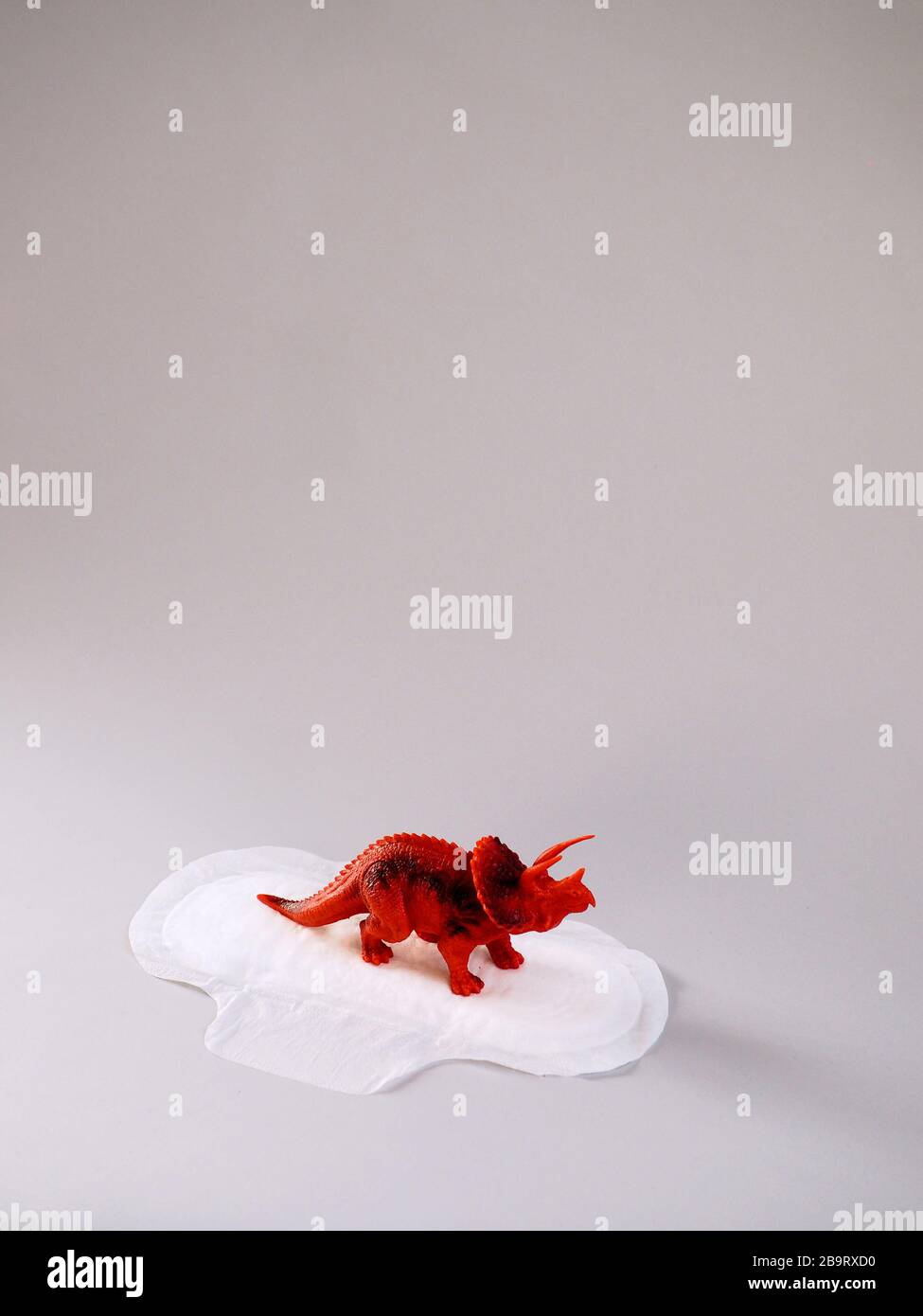 Menstrual pad with red triceratops on gray background. Minimalist still life photography concept. Women critical days, gynecological menstruation cycl Stock Photo