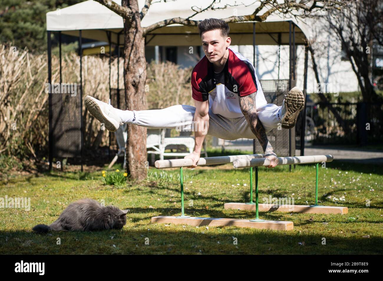 Voorzien controller Ijzig Unterhaching, Germany. 24th Mar, 2020. Marcel Nguyen, artistic gymnast,  trains on a training bar in his mother's garden. The family cat Coco sits  on the lawn. Due to the corona virus, training