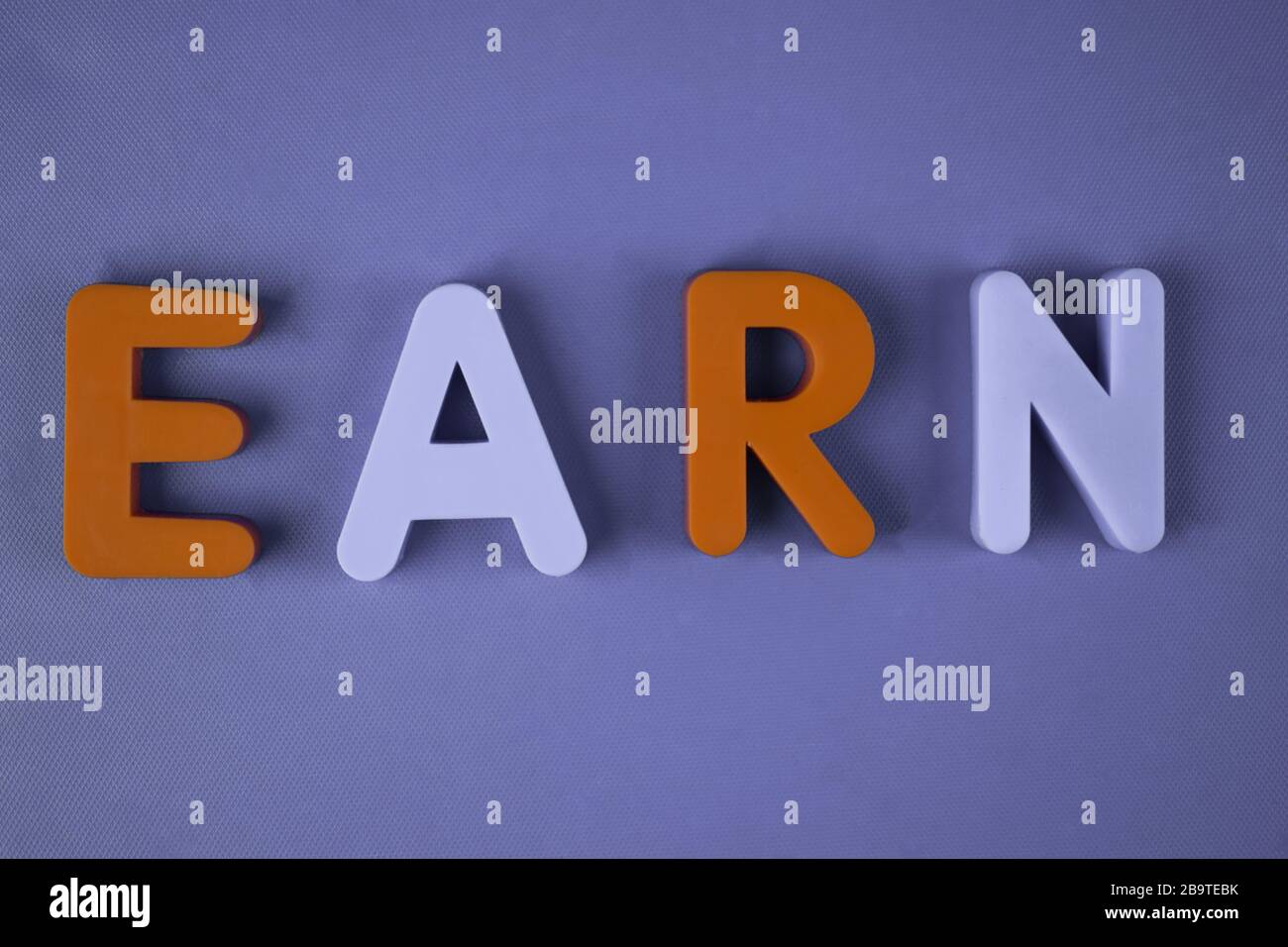 Earn word written with different colored letter blocks arranged on a light blue background Stock Photo