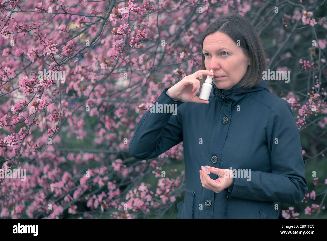 Woman using nasal spray outdoors for tree pollen allergy treatment