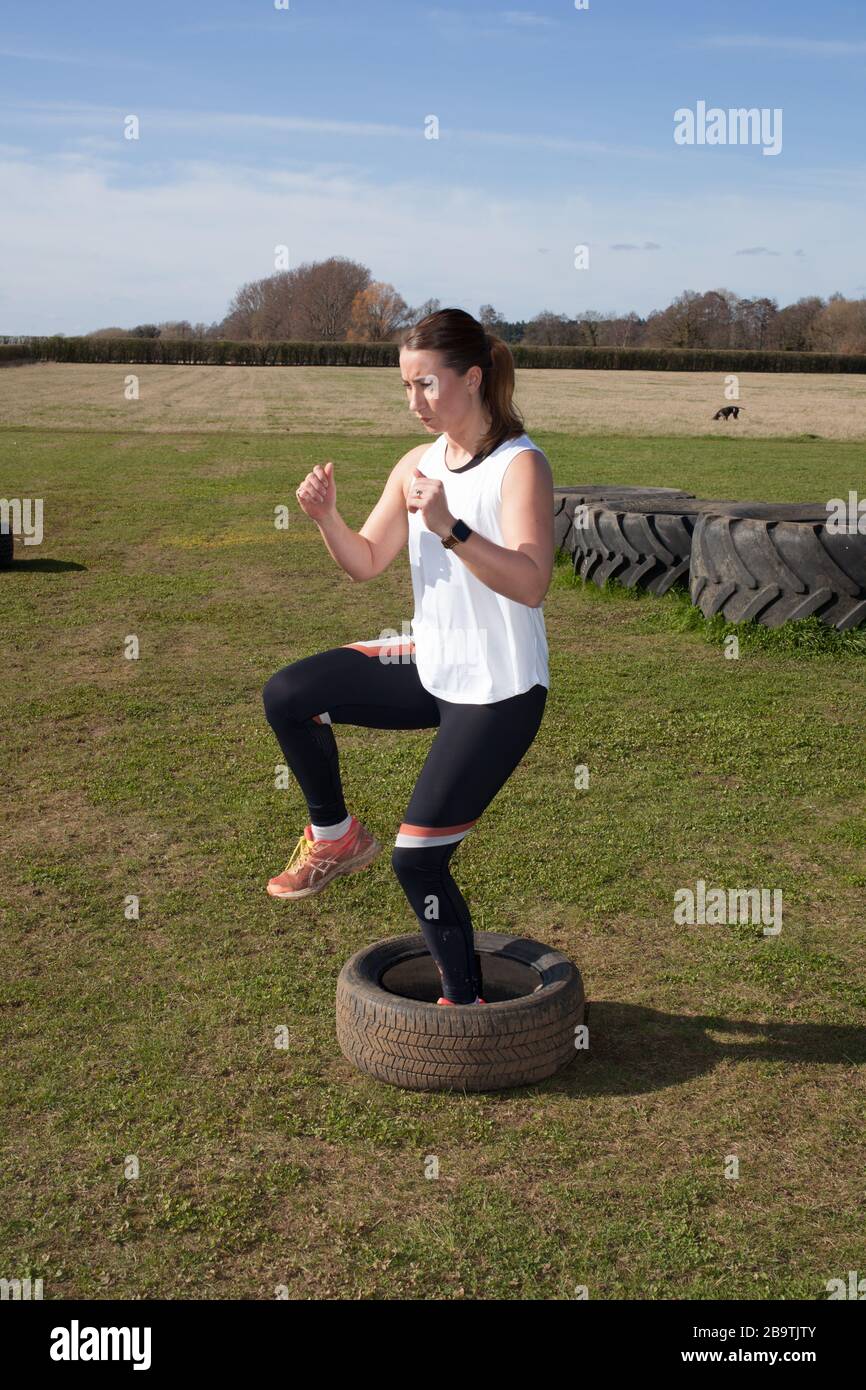 A woman exercising on a farm in the UK by doing high knees Stock Photo