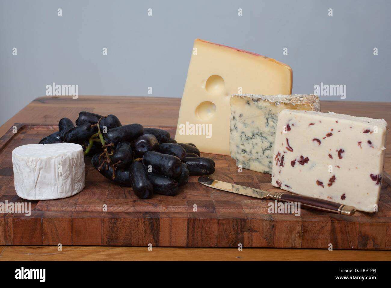 Wensleydale, Stilton, Jarlsberg and goat's cheese with black long grapes on a chopping board Stock Photo
