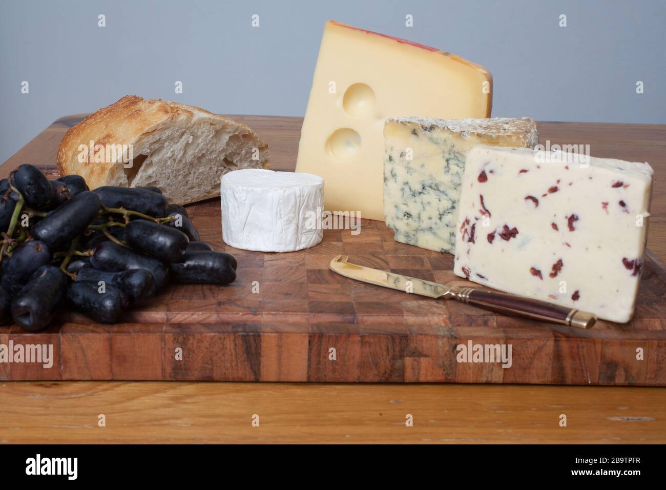Sourdough with Wensleydale, Stilton, Jarlsberg and goat's cheese with long black grapes on a chopping board Stock Photo