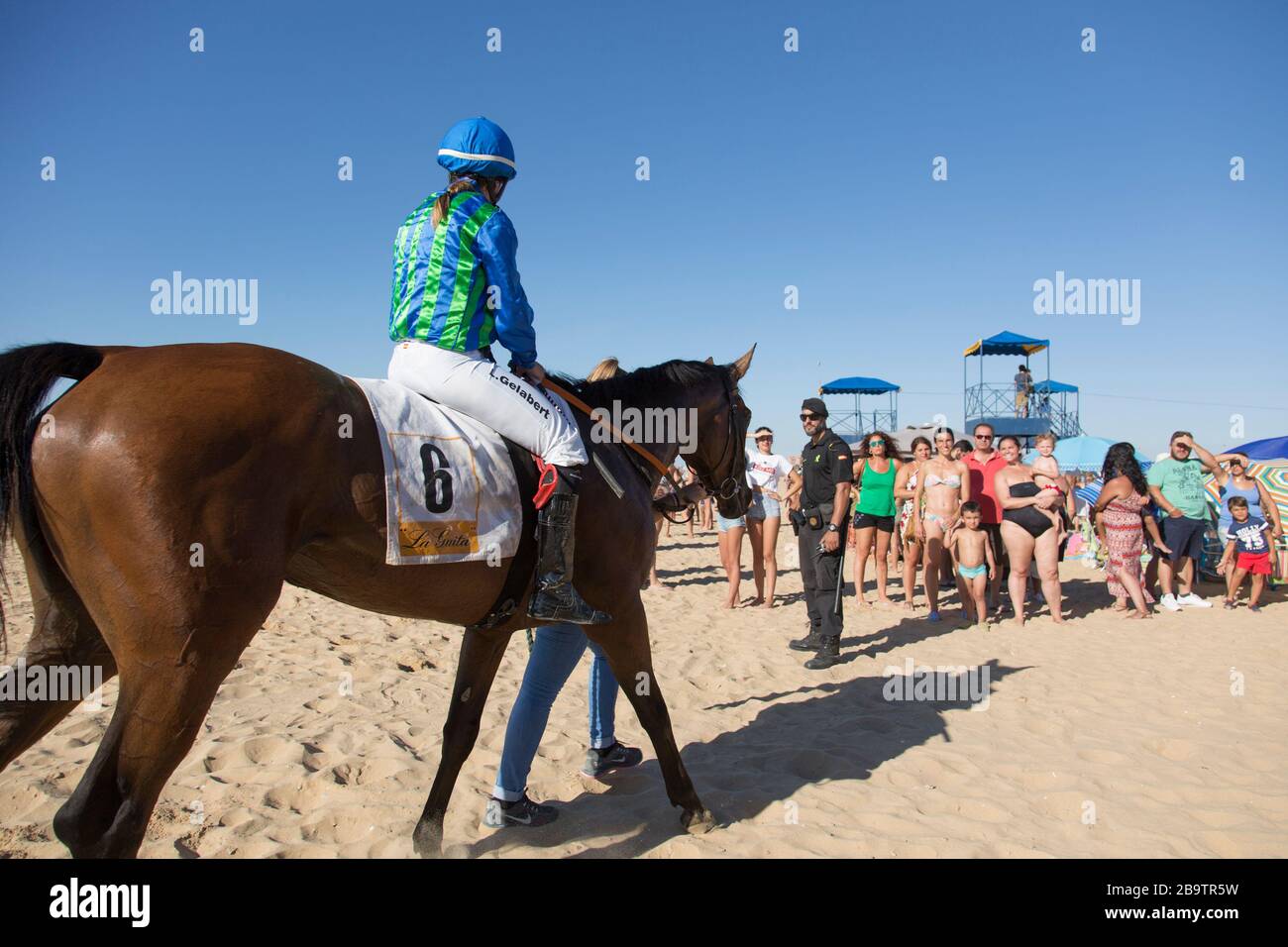 A female mounted jockey returns to the enclosure after a race during the annual August horseraces on the beach at Sanlucar de Barrameda, Cadiz, Spain Stock Photo