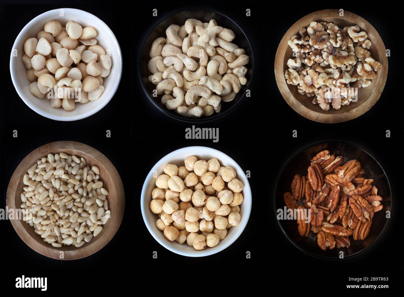 6 small bowls of nuts: Macadamias, Cashews, Walnuts, Pine nuts, hazelnuts and pecans Stock Photo
