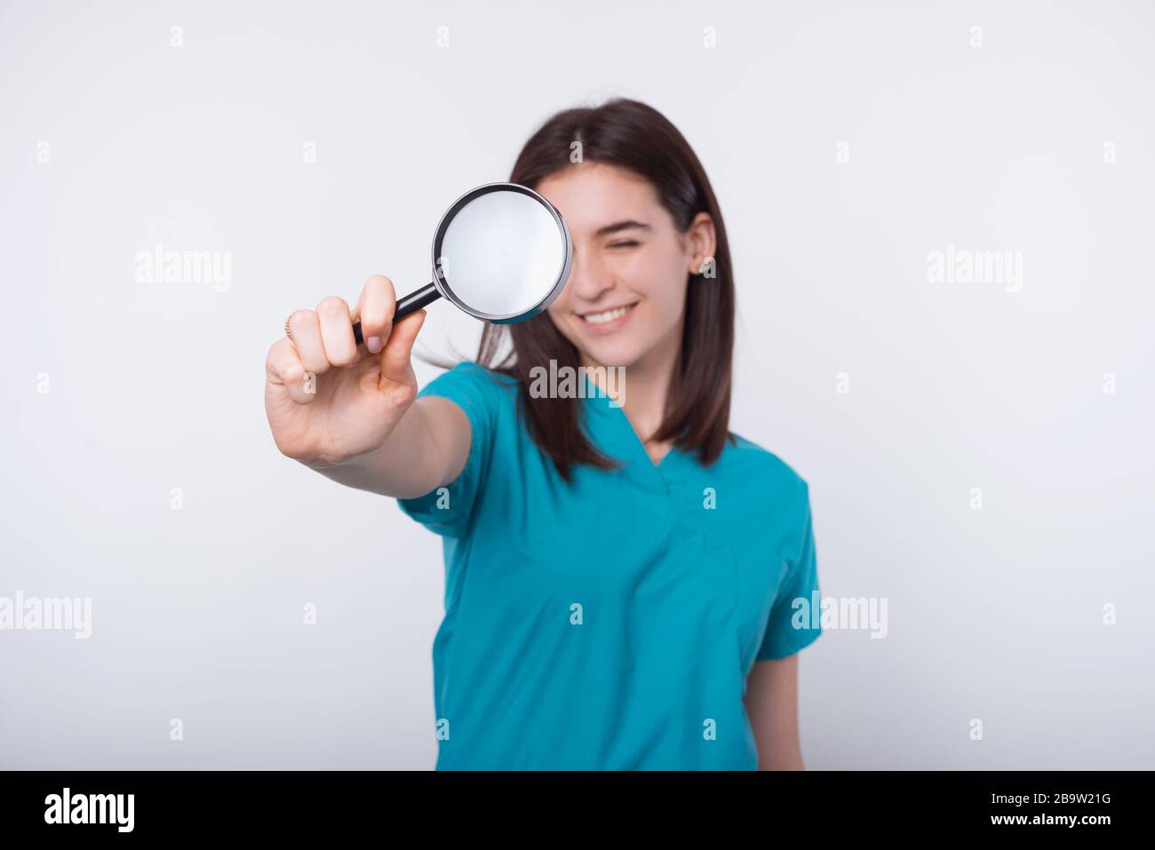 Photo of young woman doctor looking trough magnifying glass over white ...