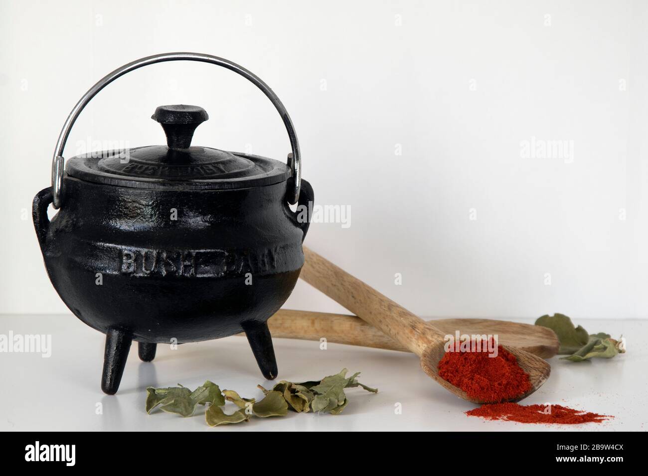Threelegged cast iron black pot, wooden spoons and paprika on white
