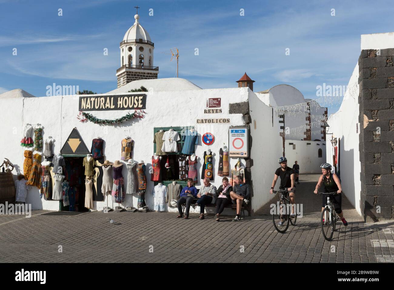 Tourists seated on a bench and on bicycles outside Natural House shop on calle Matrimonio Duque Abreut, Teguise, Lanzarote, Canary Islands, Spain Stock Photo