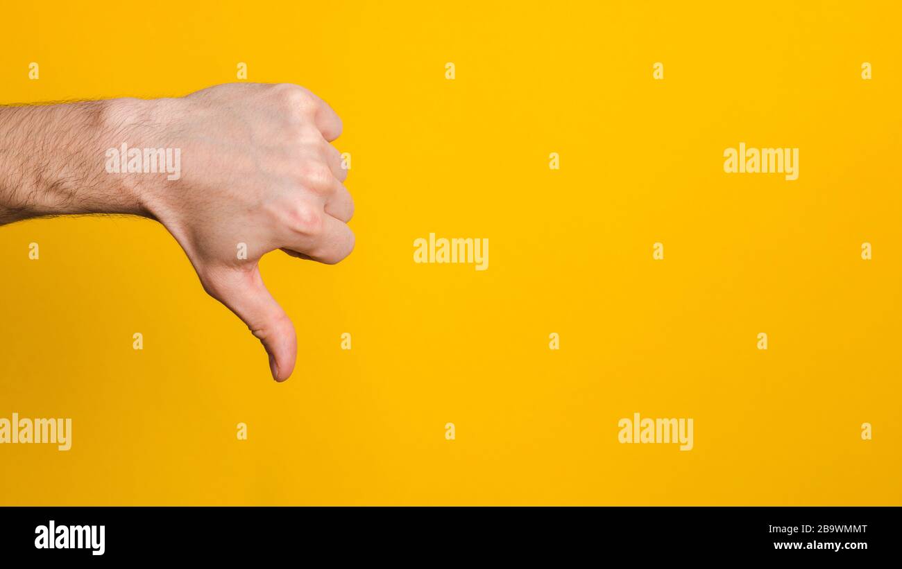 dislike sign. man hand with thumb down over yellow background with copy ...
