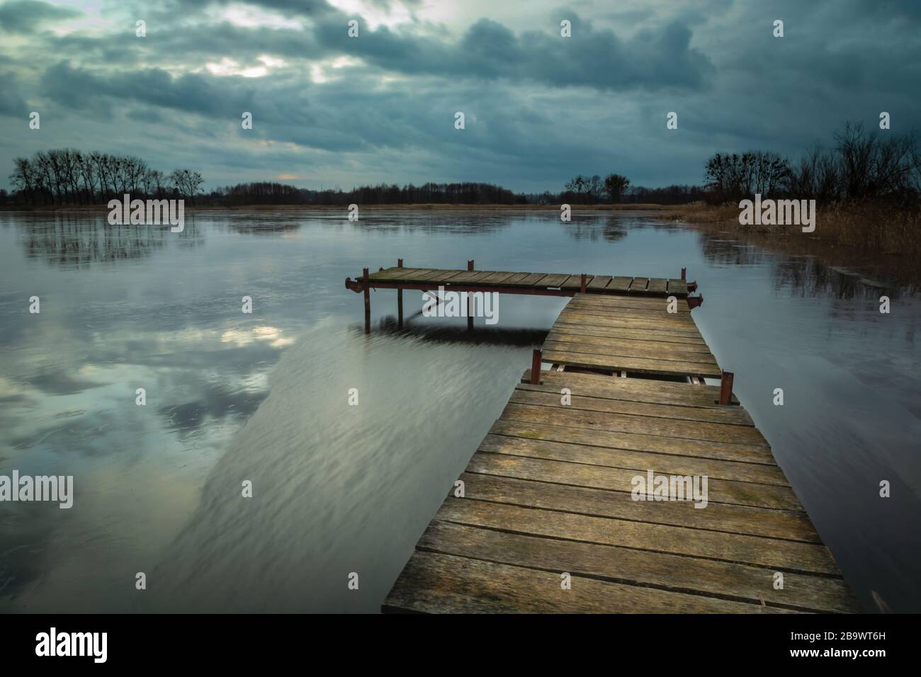 Wooden jetty on a lake and dark clouds on sky, evening view Stock Photo