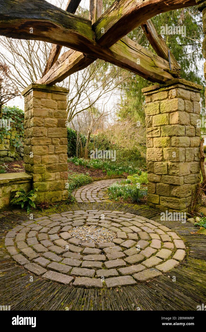 Corner of country cottage garden (rustic arbour with timber beams, stone setts, curving path, circular pattern of stones) - York Gate Garden, Leeds UK Stock Photo