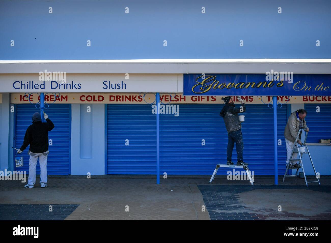 Workers maintain a safe distance as they paint traditional seaside shops on the promenade in Barry Island, Wales after Prime Minister Boris Johnson has put the UK in lockdown to help curb the spread of the coronavirus. Stock Photo