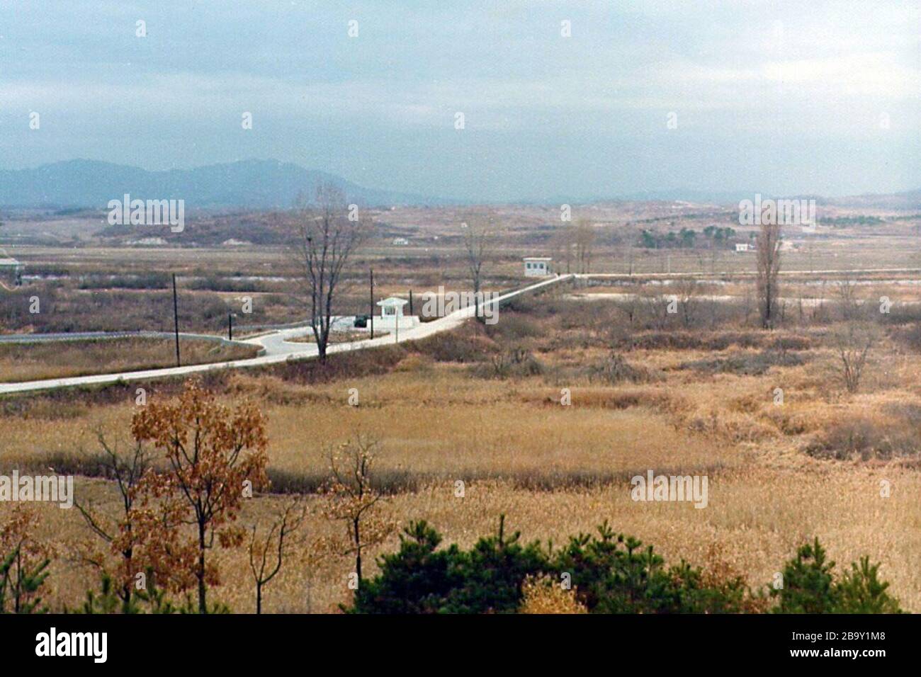 'English: I took this picture in December of 1975, from the same location the picture of the Axe Murder Incident were taken from 8 months later. At the closest end of the Bridge of No Return is CP#3, The Lonliest Outpost in the World. At the furthest end of the bridge is North Korean territory, outside of the JSA. Notice the 2 1/2 ton truck sitting at CP#3. The two people who would work there during daylight hours needed a big, heavy truck to break through the road barriers the North Koreans had erected for the occasions when they tried to block the road. Also visible in the picture is the tre Stock Photo