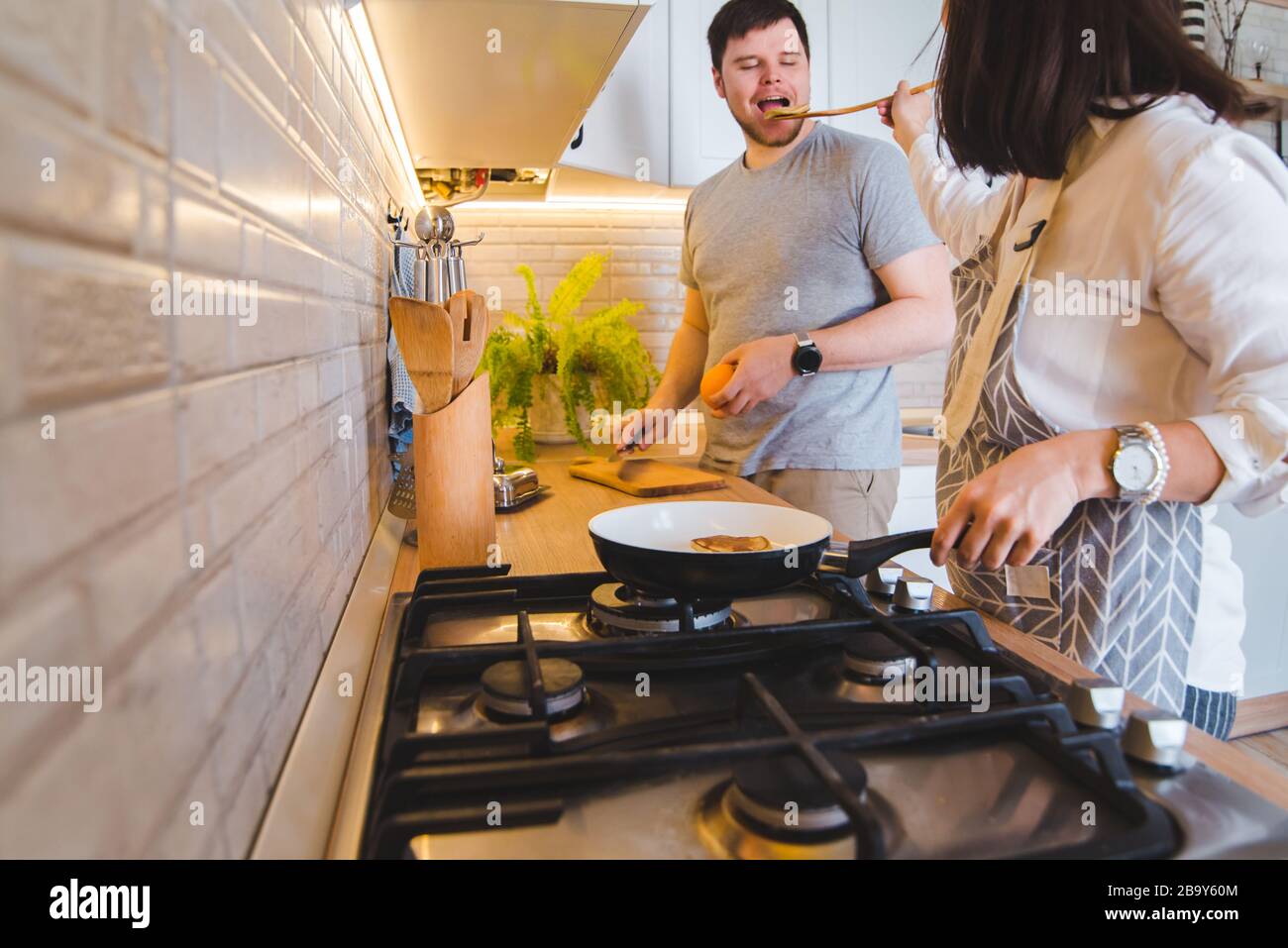 couple cooking together at the kitchen. frying pancakes cutting orange. tasting food Stock Photo