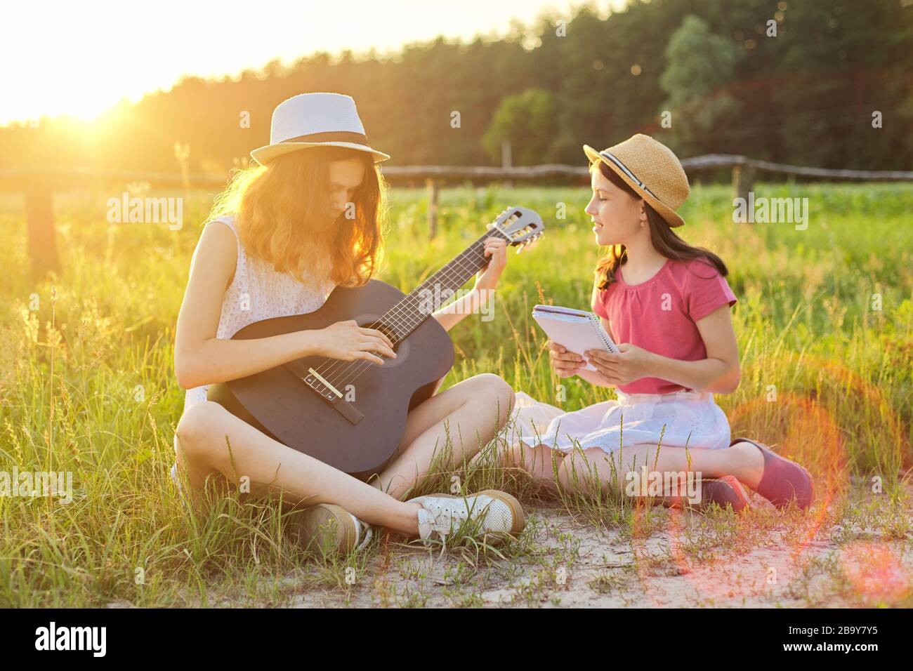 Children sitting in nature with classical guitar, two girls learning playing the guitar and