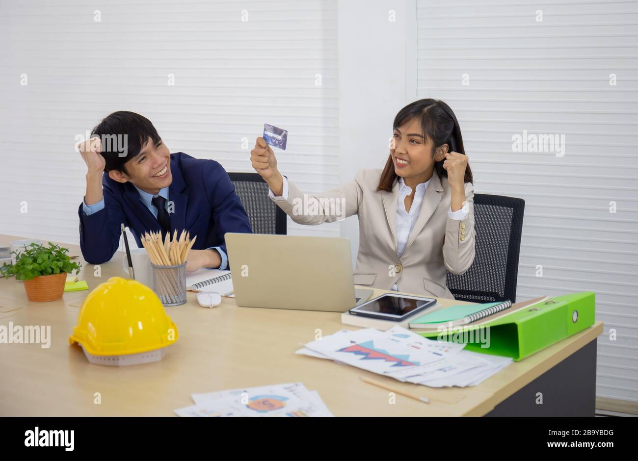 An Asian businesswoman looks happy in her hand, holding a credit card with a male staff member next to him. Stock Photo