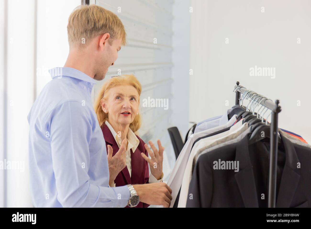 An elderly female designer is explaining information to customers about male suits. Stock Photo