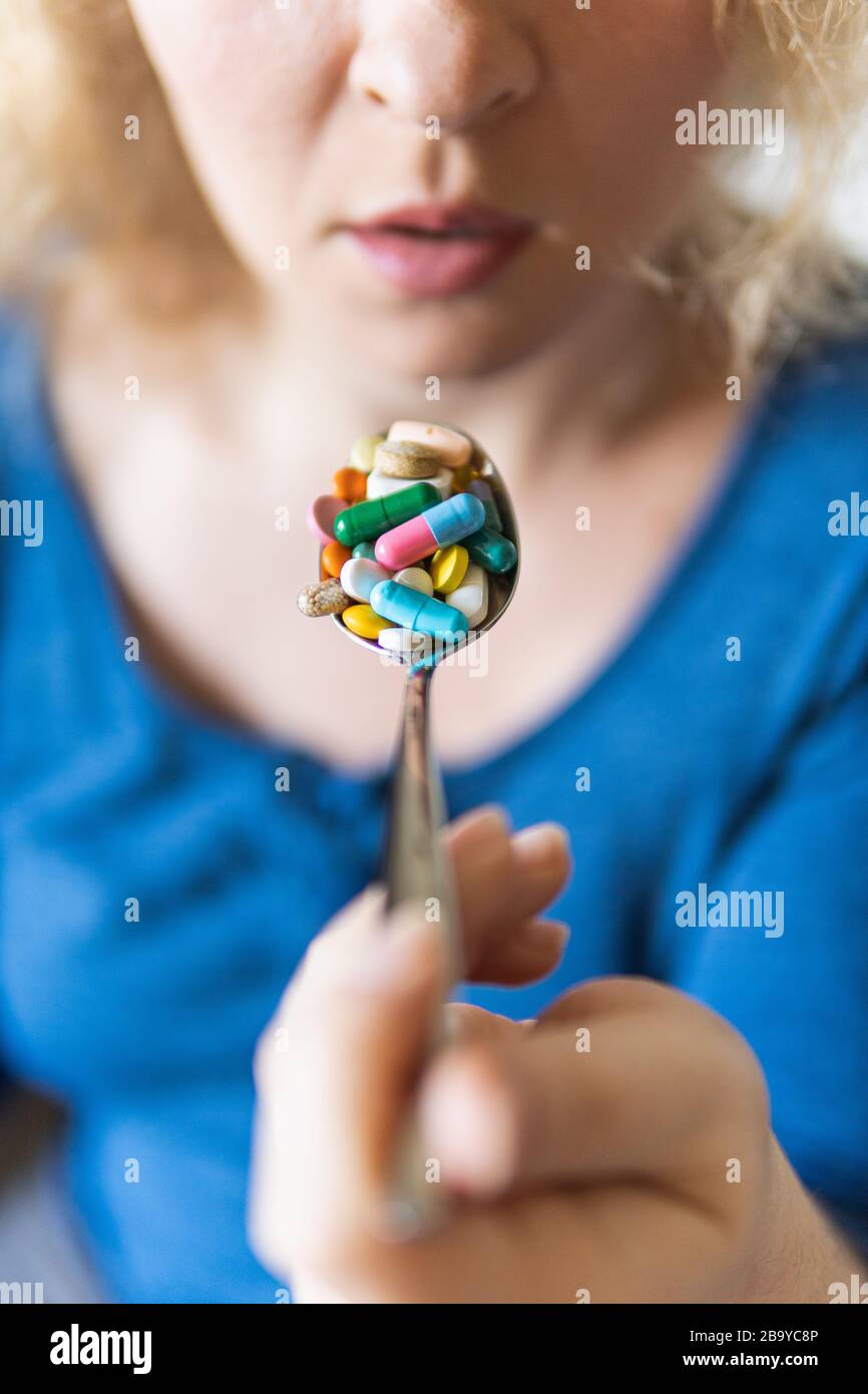 Young blonde woman holding a full spoon of assorted pills in front of her open mouth. Stock Photo