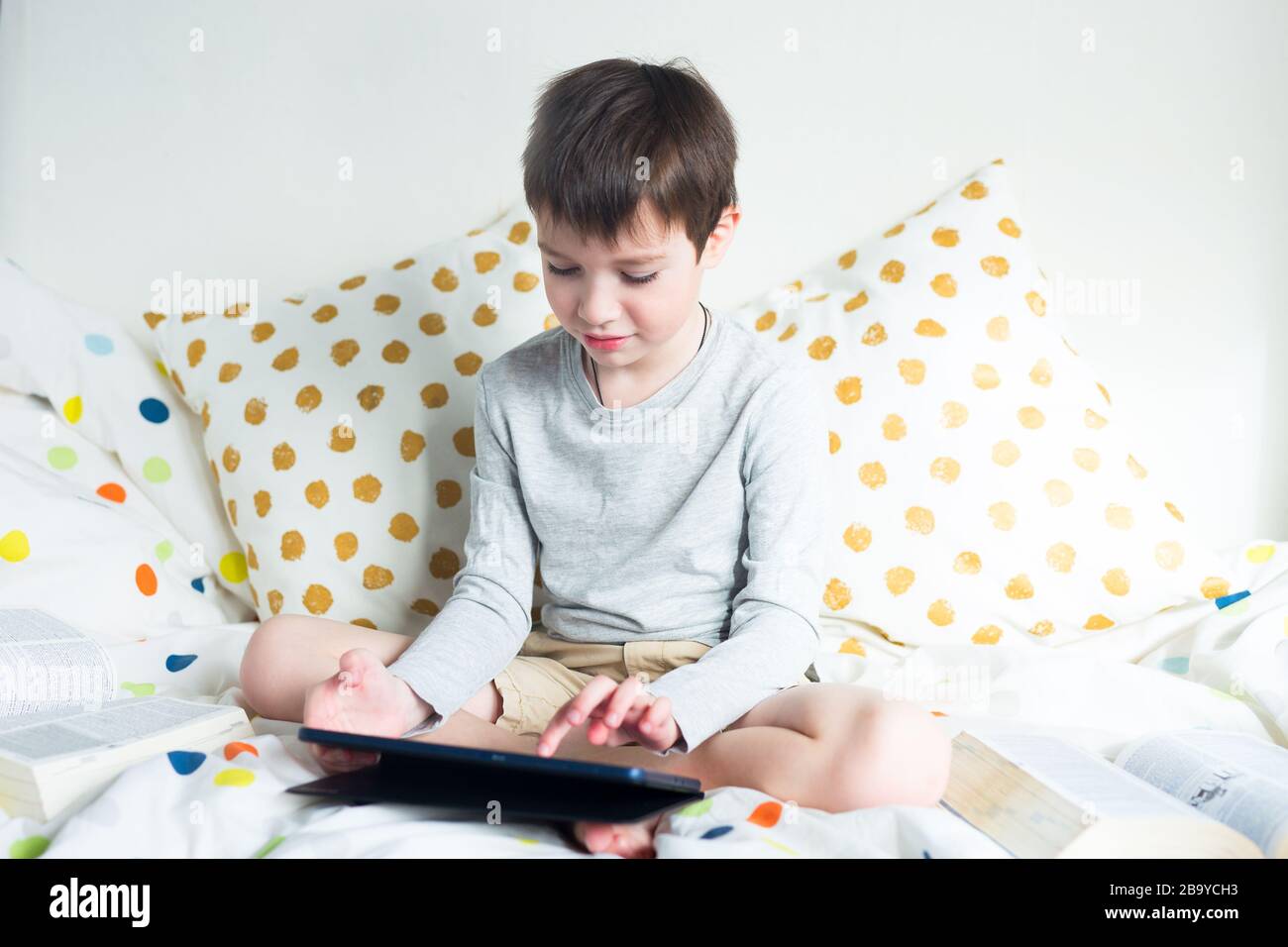 School Boy on bed at home with digital tablet in hand, doing homework