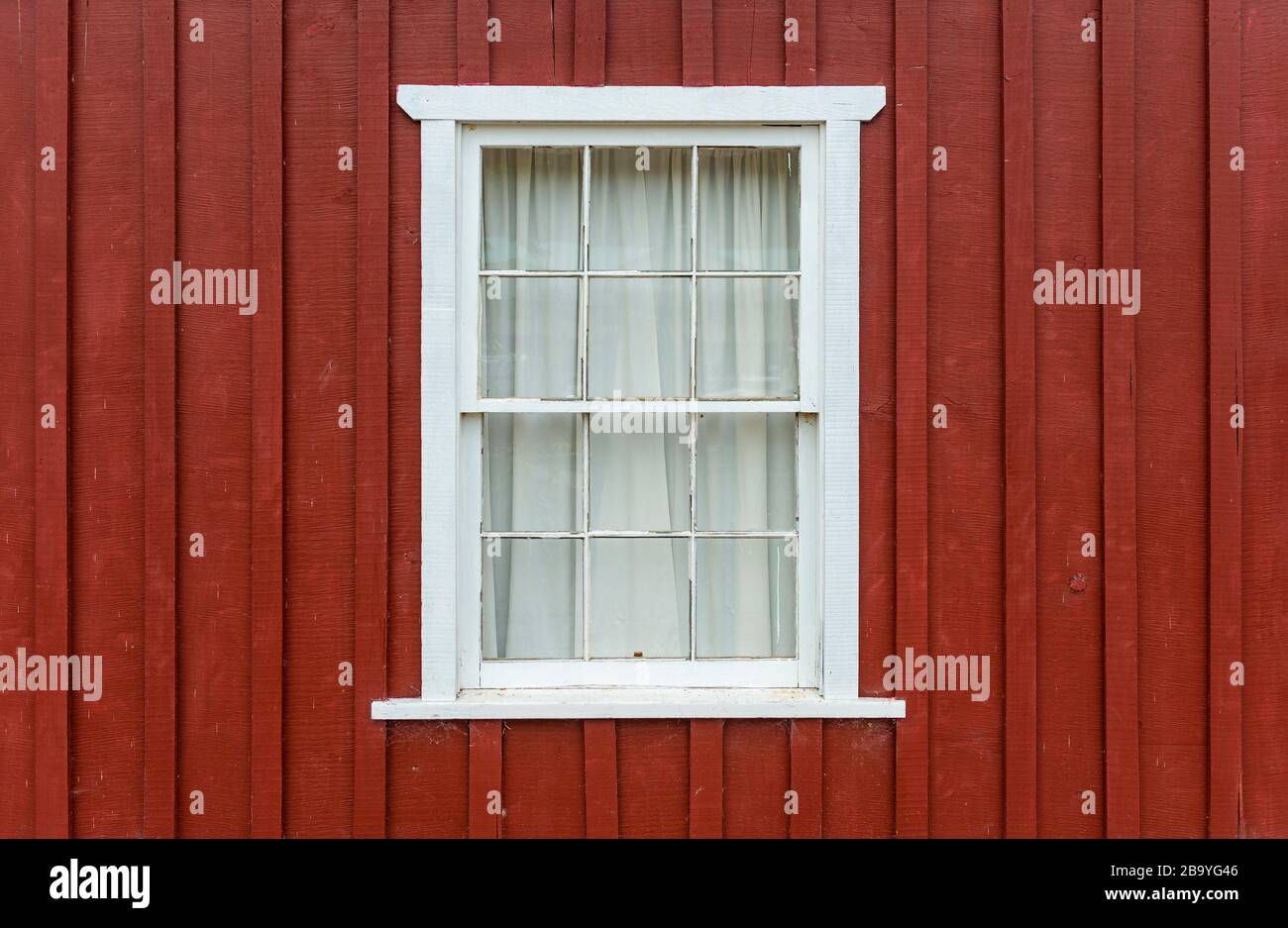 Facade with red brown colored wood and a white window frame with curtain, Telegraph Cove, Vancouver Island, British Columbia, Canada. Stock Photo