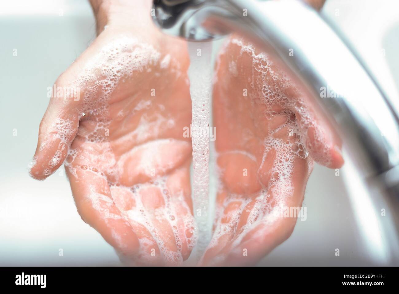 Hands under running sink faucet washing with soap and warm water. Stock Photo