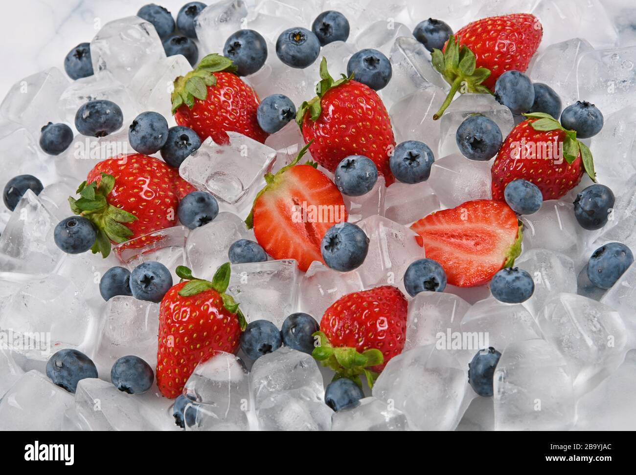 Close up fresh red ripe strawberries, blueberries and ice cubes on table, high angle view Stock Photo