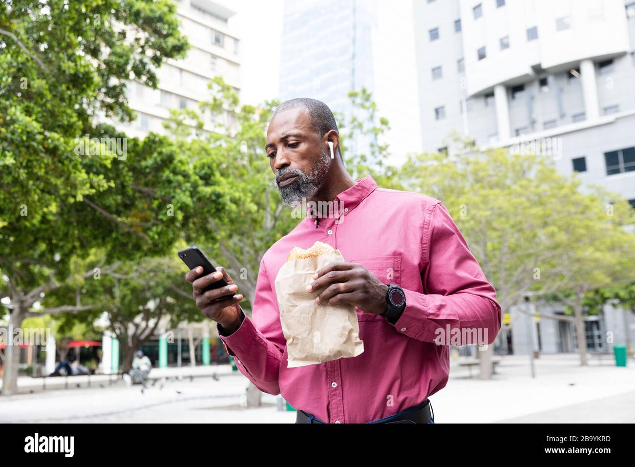 African American man using his phone and eating a takeaway sandwich Stock Photo