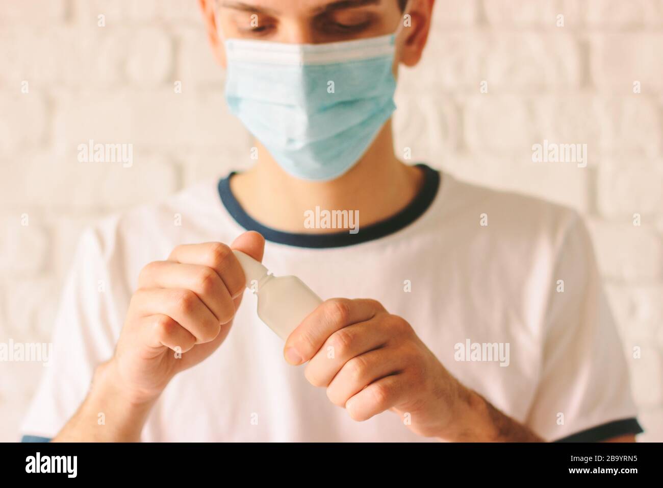 Portrait of young sick man with runny nose using nasal spray. Confident ill man doctor in medical face mask holding nose drops for congested nose. Pan Stock Photo