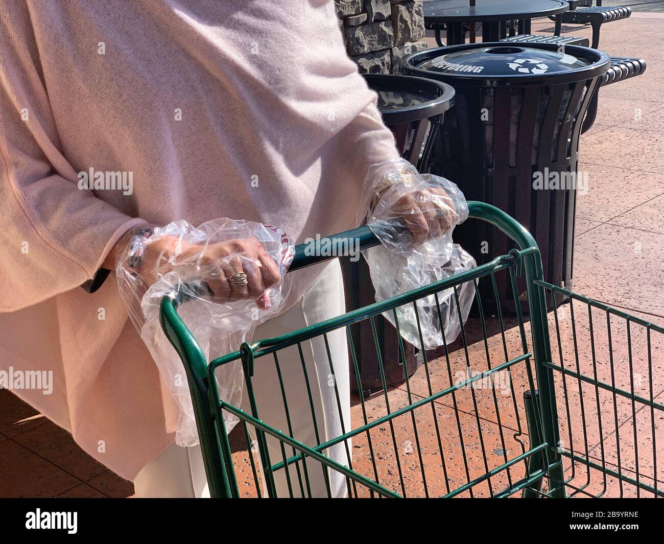 Young woman uses plastic bags as gloves to prevent contact with Coronavirus while grocery shopping. Stock Photo