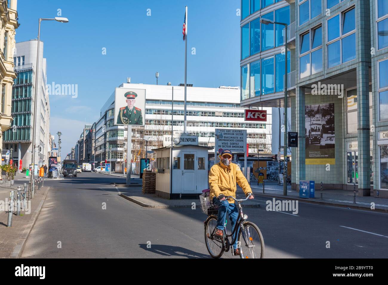 Man wearing face mask cycles past Checkpoint Charlie, one of Berlin's main tourist attractions, deserted during lockdown in the corona crisis Stock Photo