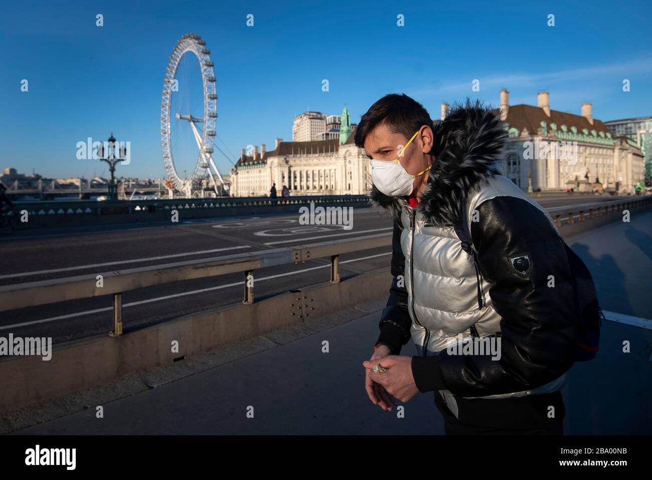 A man in a protective face mask walks on Westminster Bridge, London, in the normally busy evening rush hour after Prime Minister Boris Johnson made the decision to put the UK in lockdown to help curb the spread of the coronavirus. Stock Photo
