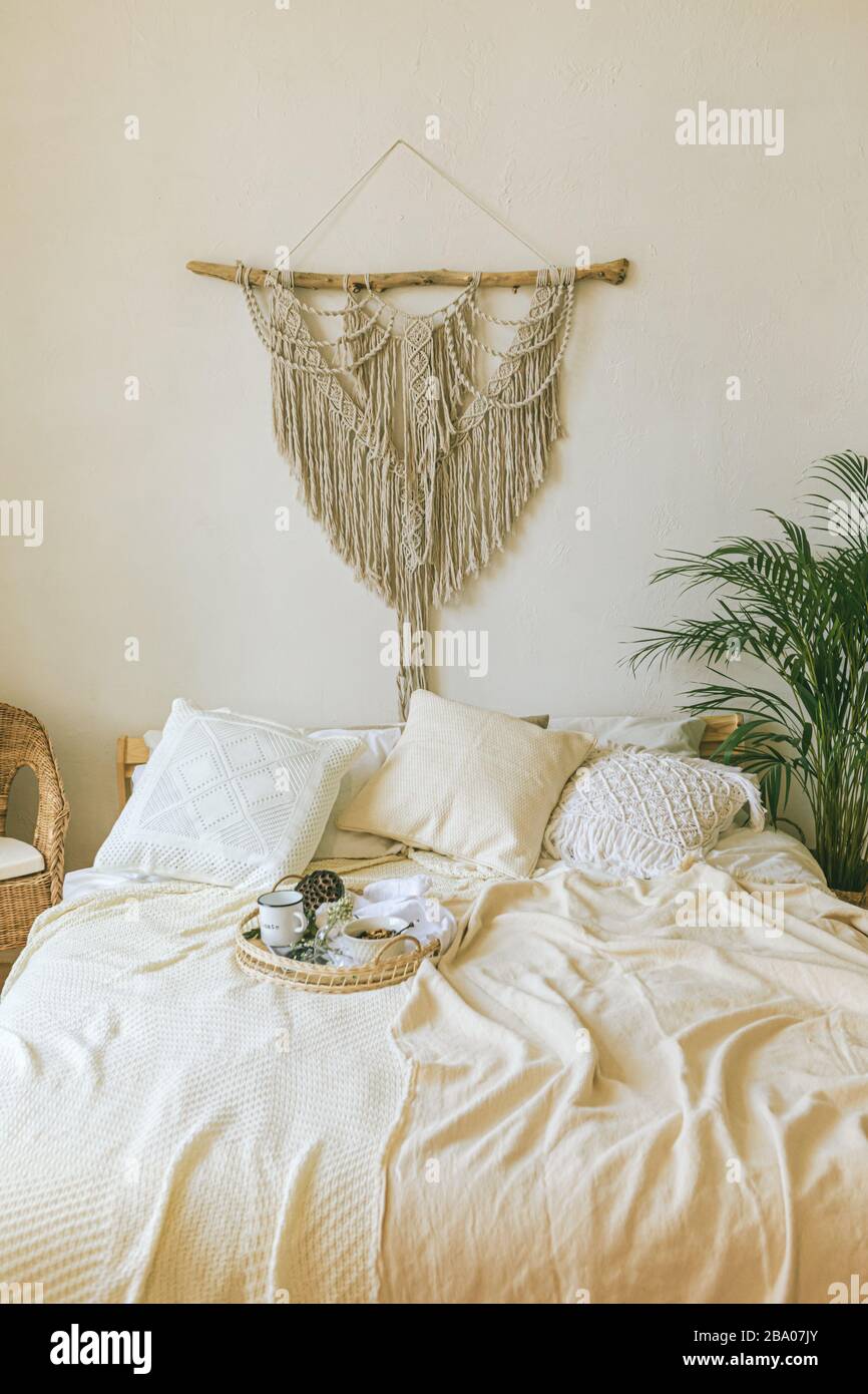 Modern romantic scandi boho style bedroom interior with decorative pillows, green plant and diy macrame wall panel. Light warm cozy comfortable home. Stock Photo