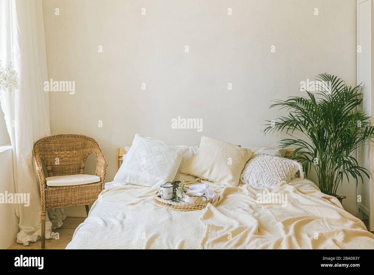 Modern romantic scandi boho style bedroom interior with decorative pillows, green plant and empty wall for poster or art mock-ups. Light warm cozy com Stock Photo