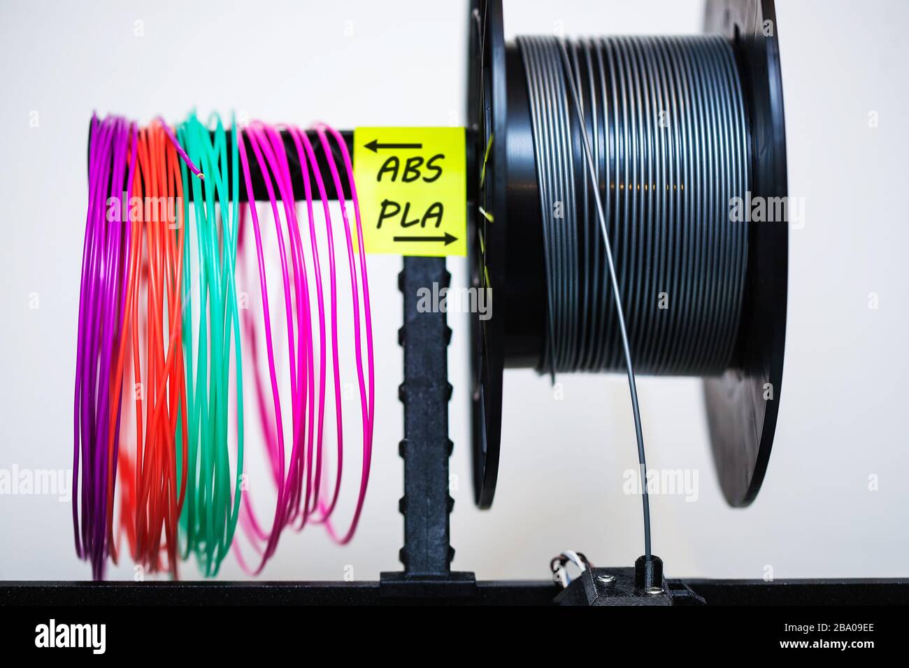Loaded plastic filament on extruder with a sticky note that labels the variety of plastics used in 3d printing. Stock Photo