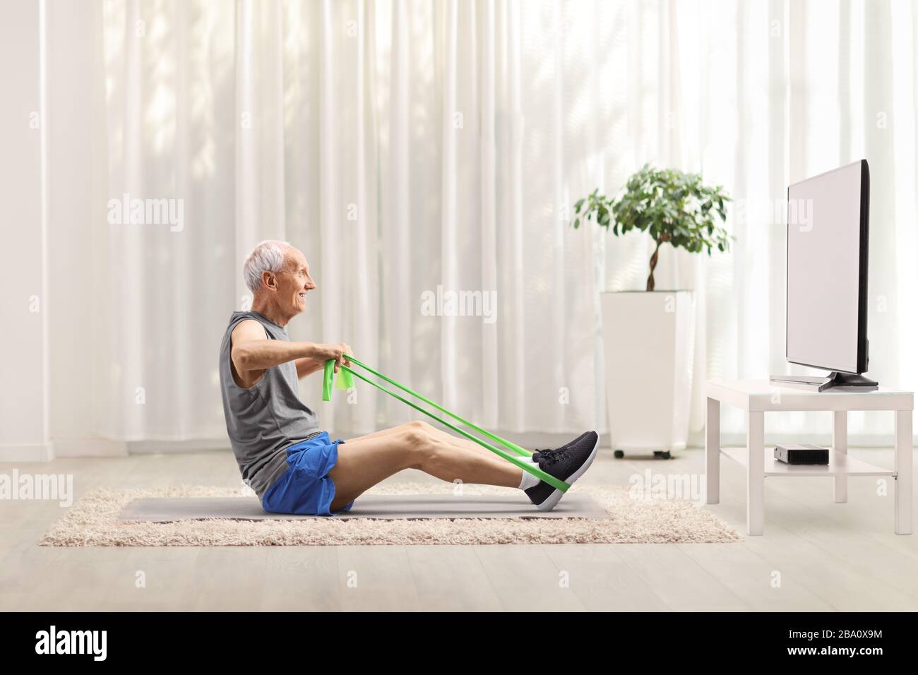 Elderly man exercising with an elastic band in front of a tv at home Stock Photo