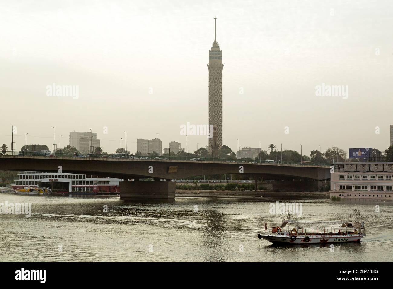 A boat on the River Nile by the 6th October Bridge in Cairo, Egypt. The Cairo Tower, known as Nasser's Pineapple, dominates the urban landscape. Stock Photo